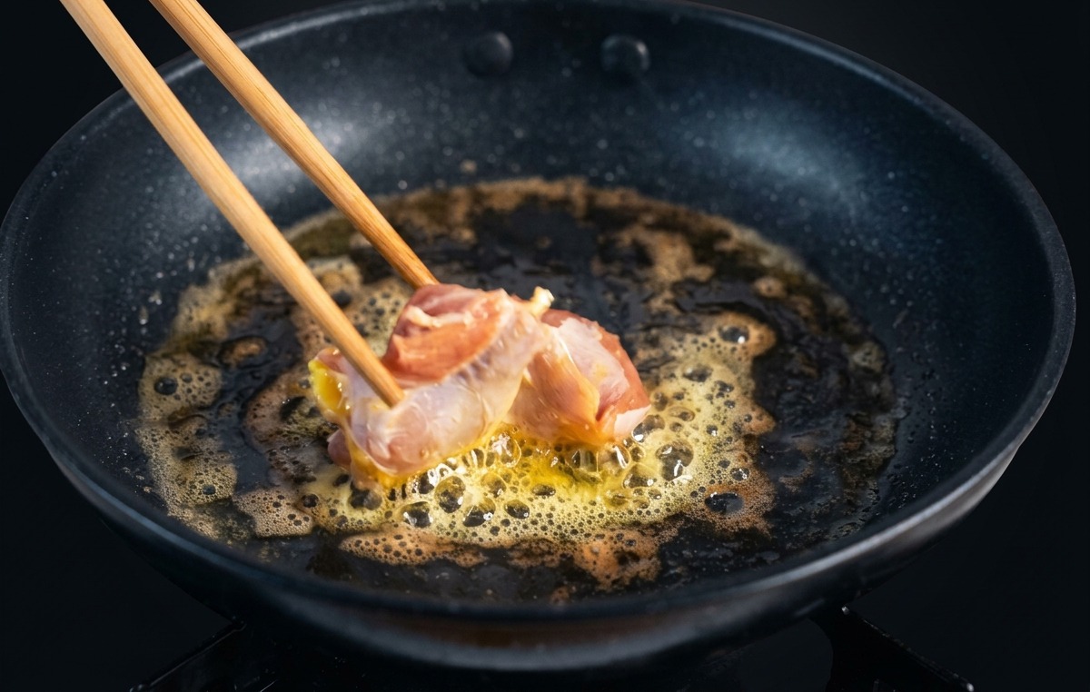 泡立つ溶かしバターが入ったフライパンに、木箸で生のピンク色の鶏もも肉を並べている様子。