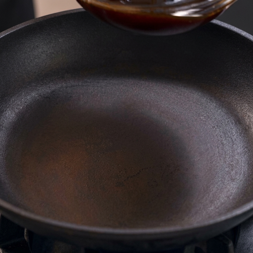 コンロの上の黒いフライパンに、混ぜ合わせた親子丼のタレを注ぎ入れている様子