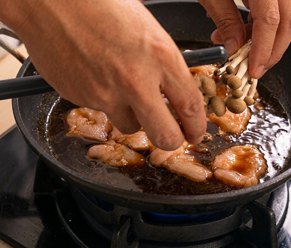 煮立つタレの中に、一口大の鶏肉としめじの株を丁寧に並べて入れている様子