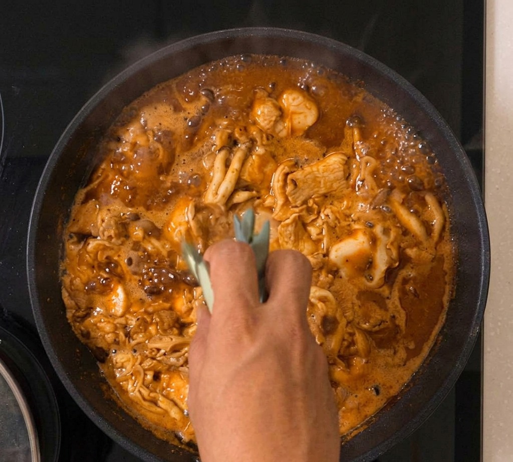 フライパンの中で卵が固まりつつある親子丼に、細かく刻んだ青ねぎが散りばめられている様子