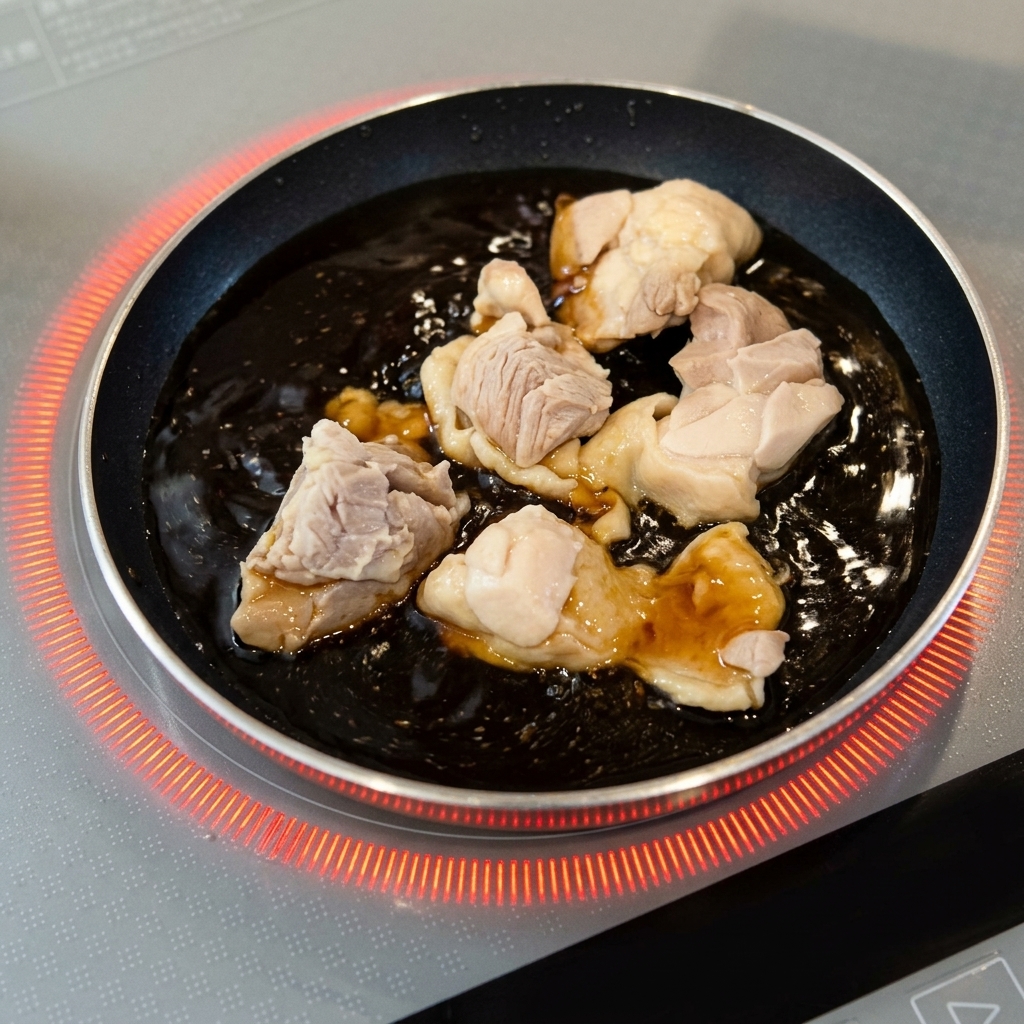 小さな丸いフライパンの中で、ふつふつと泡立つ濃い茶色のタレと一緒に煮込まれている下茹で済みの鶏肉。