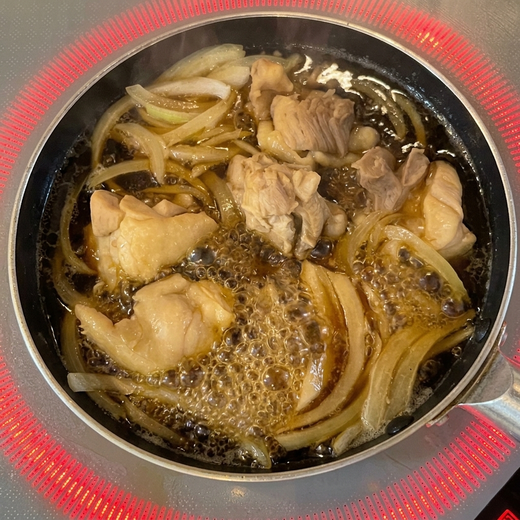 ボウルから、鶏肉と玉ねぎが入ったフライパンへ溶き卵が回し入れられている様子。