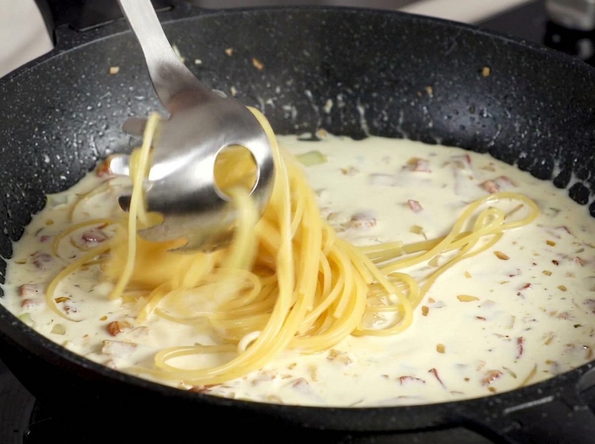 茹で上がったスパゲッティをソースが入ったフライパンに移す様子。