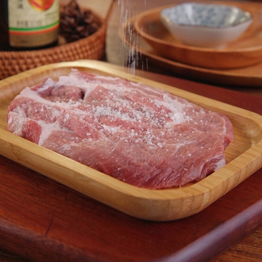 木製のトレイにのせた生の豚肉に塩を振っている様子