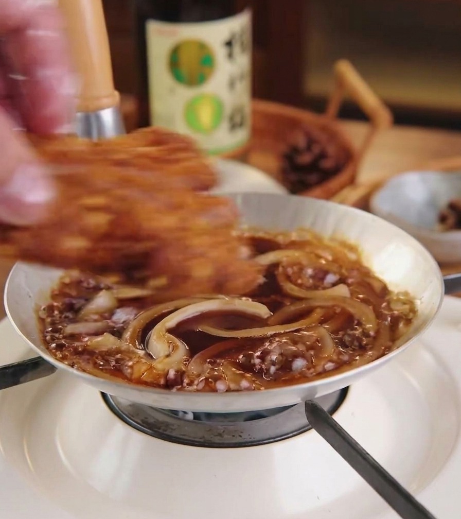 小さめの鍋で煮立っている玉ねぎと煮汁の上に、揚げたてのトンカツを並べている様子
