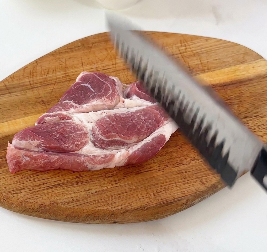 まな板の上で包丁の背を使って豚肉を叩いている様子。