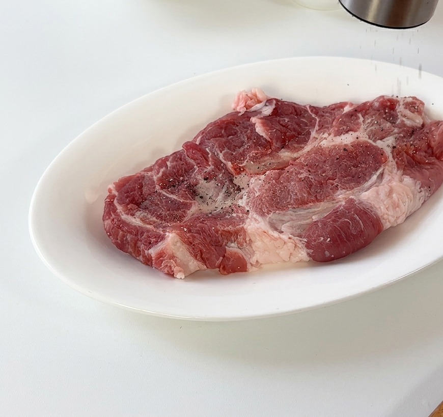 白いお皿にのせた豚肉に黒こしょうを挽き入れている様子。