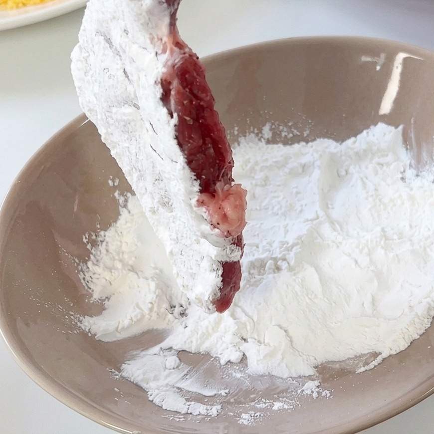 ボウルに入った薄力粉を豚肉にまぶしている様子。