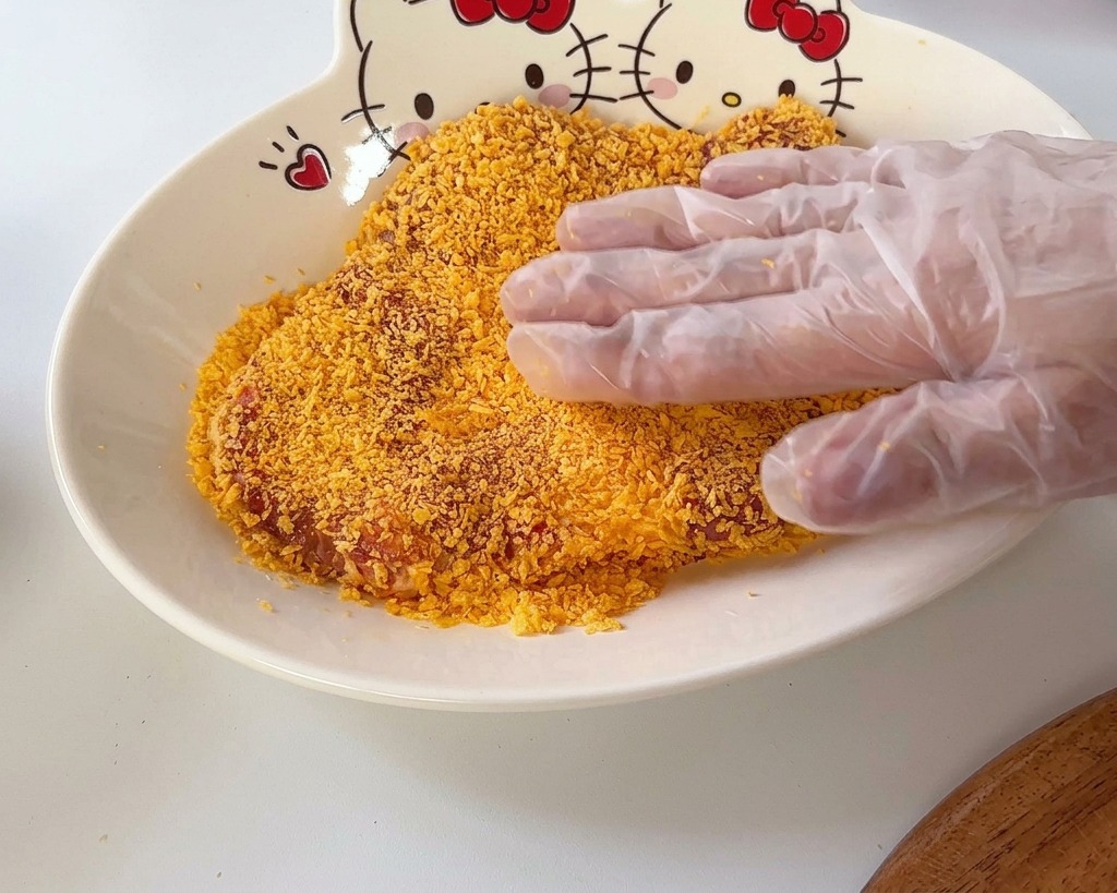 ハローキティ柄のボウルに入ったオレンジ色のパン粉に、豚肉を押し当てている様子。