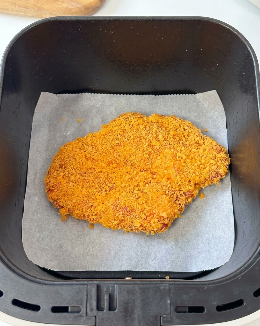 クッキングシートを敷いたノンフライヤーのバスケットに、衣をつけた豚肉を入れている様子。