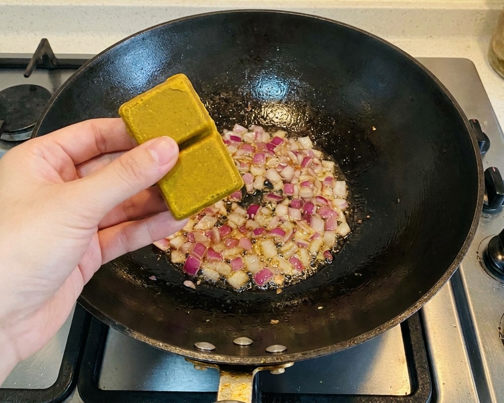 炒めた紫玉ねぎの入った鍋に、カレールーを2つ入れている様子。