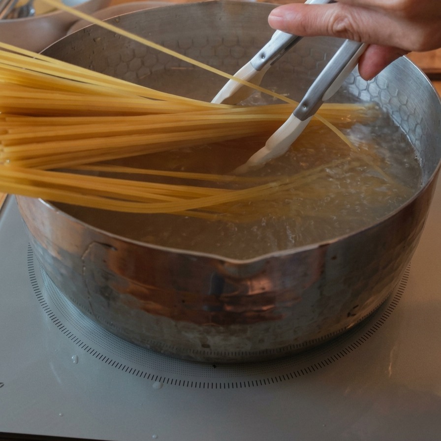 沸騰した鍋の湯にトングを使ってスパゲッティを沈めている様子。