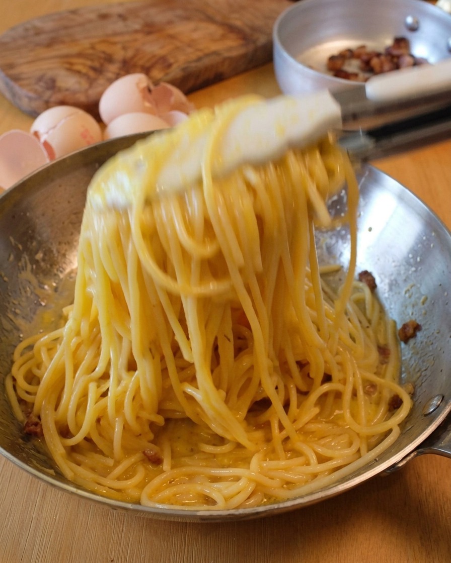 トングを使ってフライパンの中でパスタを大きく回し、全体にソースを馴染ませている様子。