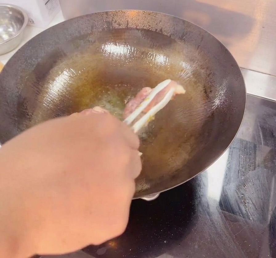 トングを使って黒い中華鍋の中で鶏もも肉をひっくり返し、カリッと香ばしい黄金色に焼けた皮目を見せている様子。