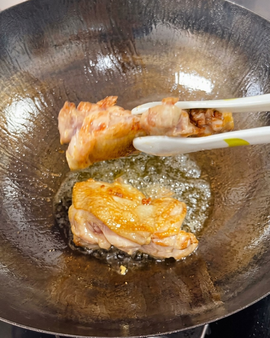 中華鍋の中でトングを使って、カリッと香ばしく焼けた鶏もも肉をひっくり返している様子。