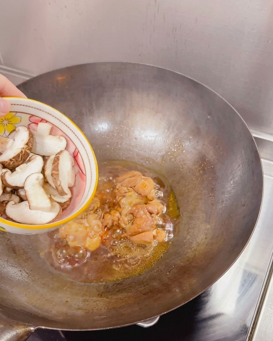 焼き付けた鶏肉とフツフツと泡立つタレが入った中華鍋に、ボウルからスライスした新鮮な椎茸を加えている様子。