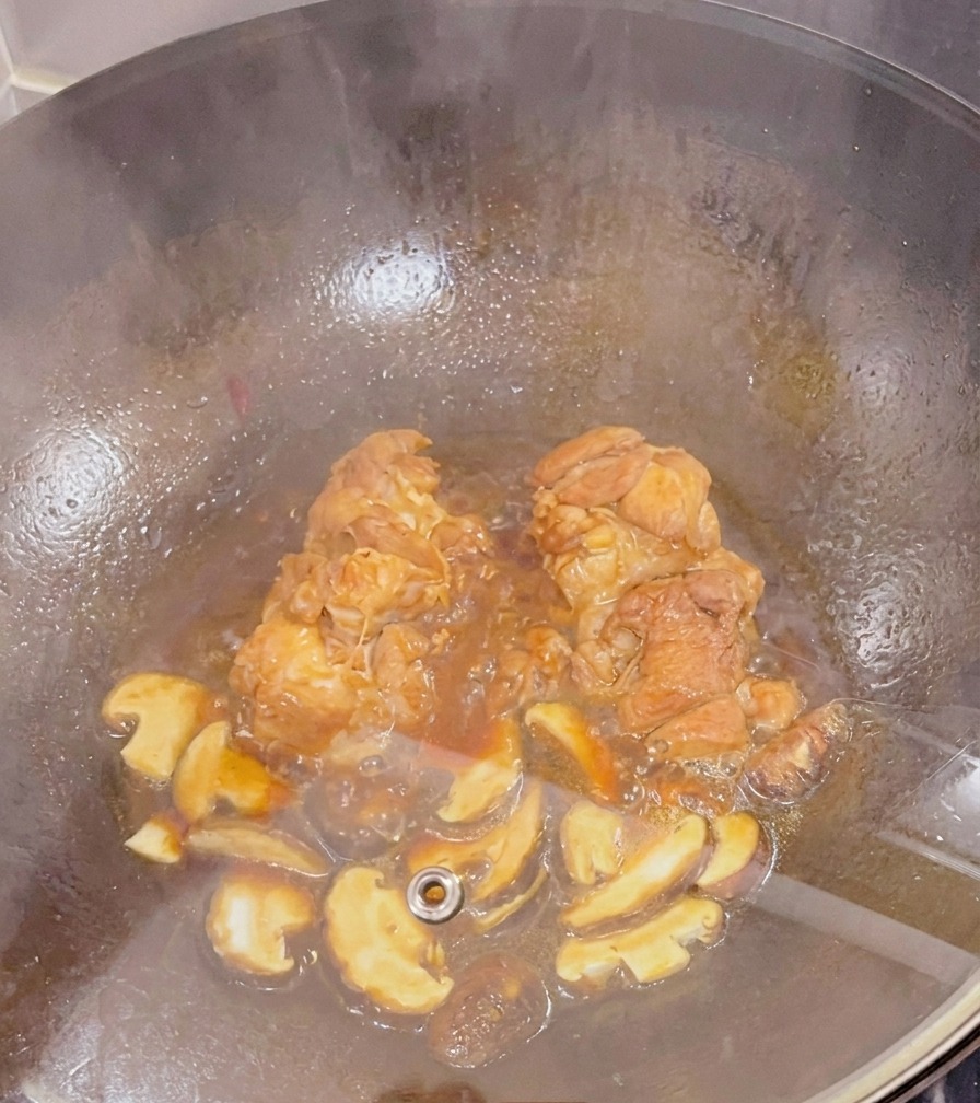 ガラスのフタをした中華鍋の中で、濃いタレと一緒にグツグツと煮込まれている鶏もも肉とスライスした椎茸の様子。