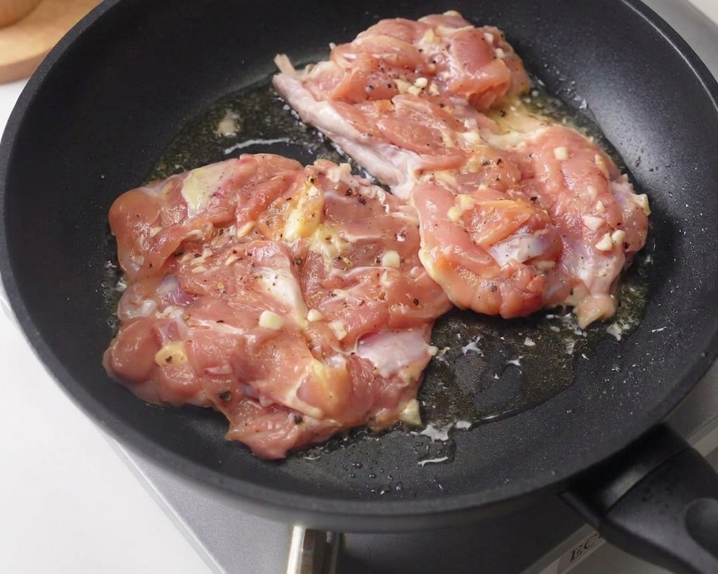 黒いフライパンの中で、下味をつけた鶏もも肉2枚を皮目を下にして弱火で焼いている様子。
