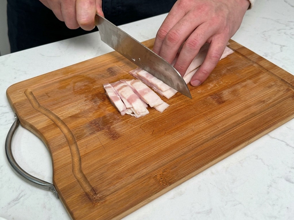 まな板の上で厚切りのベーコンを細切りにする様子