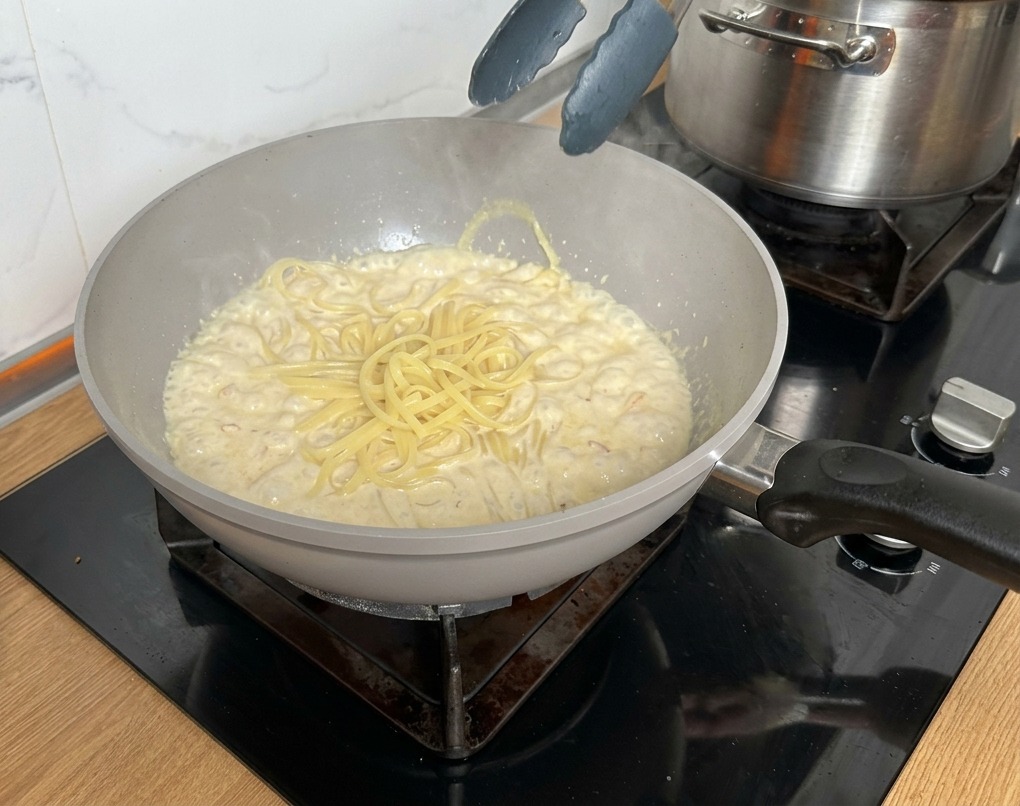 トングを使って茹で上がったパスタをソースの入ったパンに移す様子