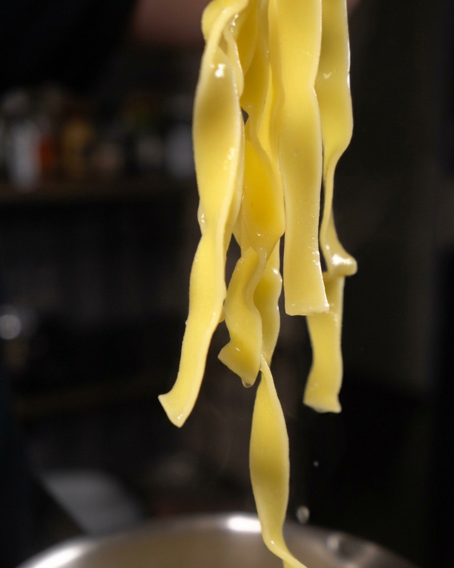 トングで掴み上げられた、水気が滴る黄色いタリアテッレパスタ