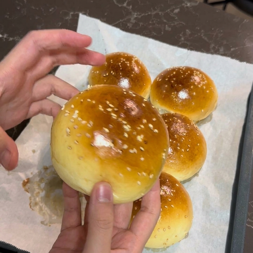 焼き上がったばかりの黄金色で白ごまがたっぷりのバンズを両手で優しく持っている様子。