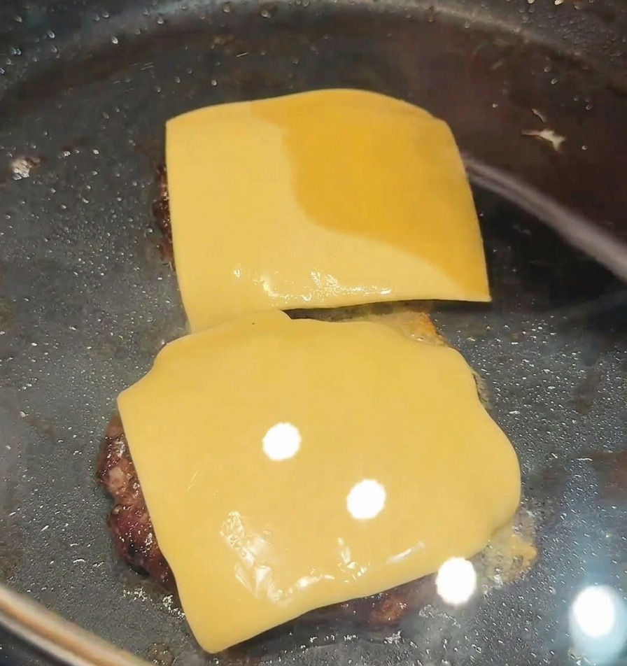 フライパンに蓋をして、パティの上のチーズを蒸らし溶かしている様子。
