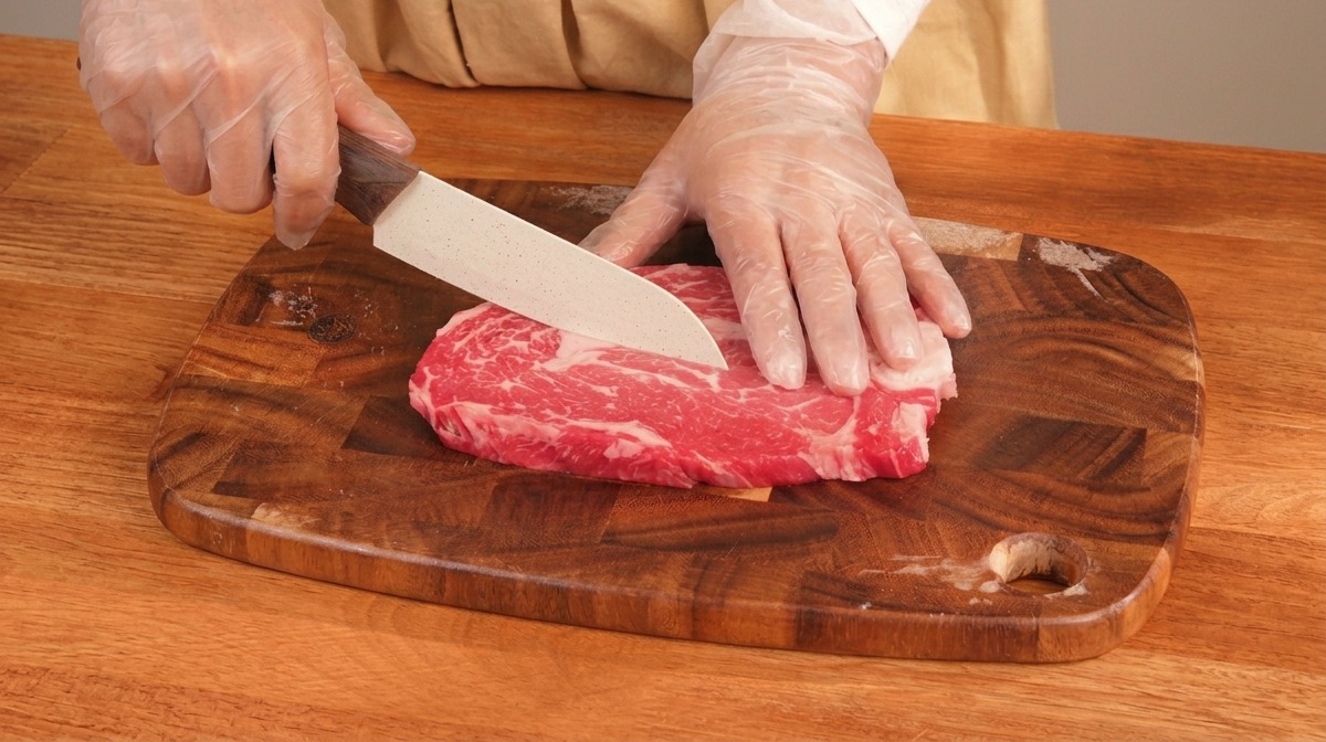 木製のまな板の上で、霜降りのステーキ肉を一口サイズに切り分けている様子。