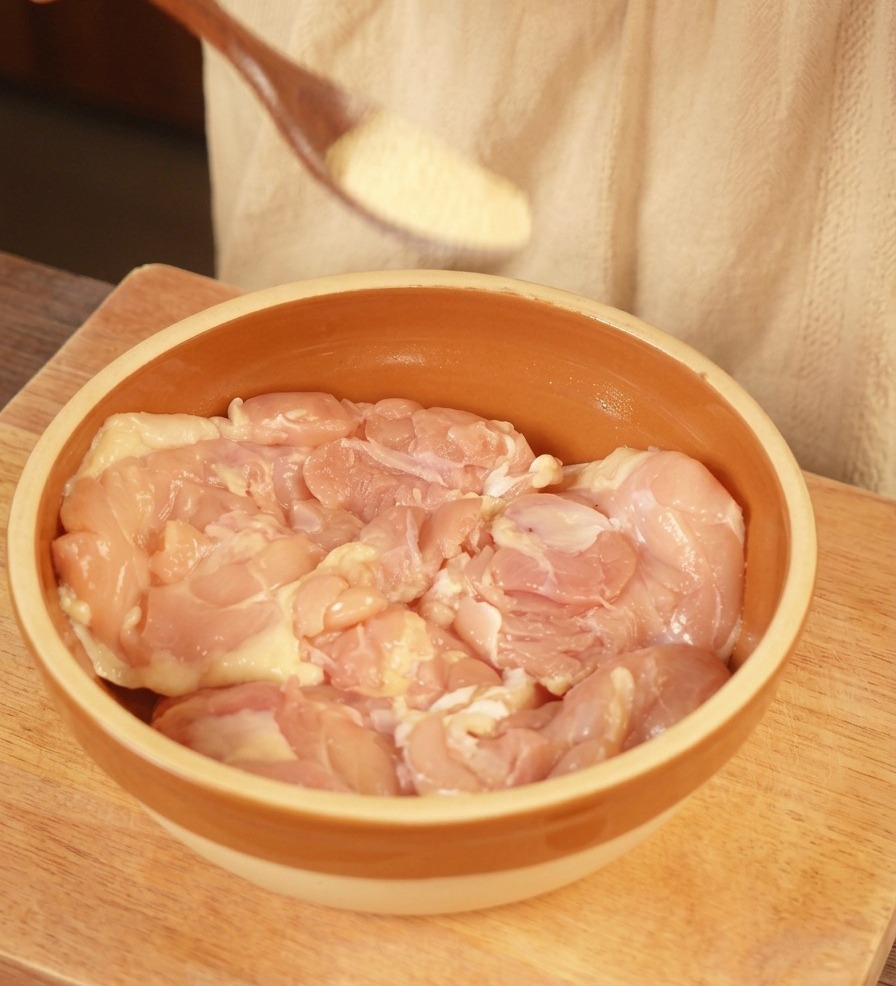 茶色のボウルに入った鶏もも肉に、ガーリックパウダーを振りかけている様子