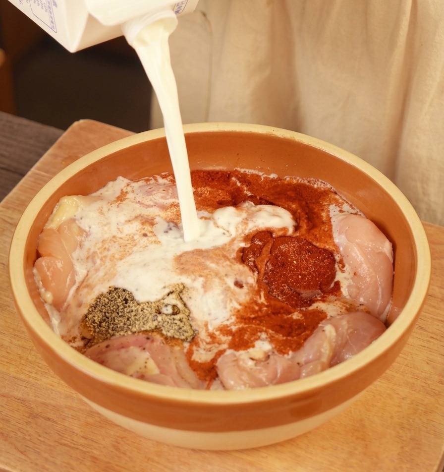 味付けした鶏もも肉に牛乳を注いでいる様子
