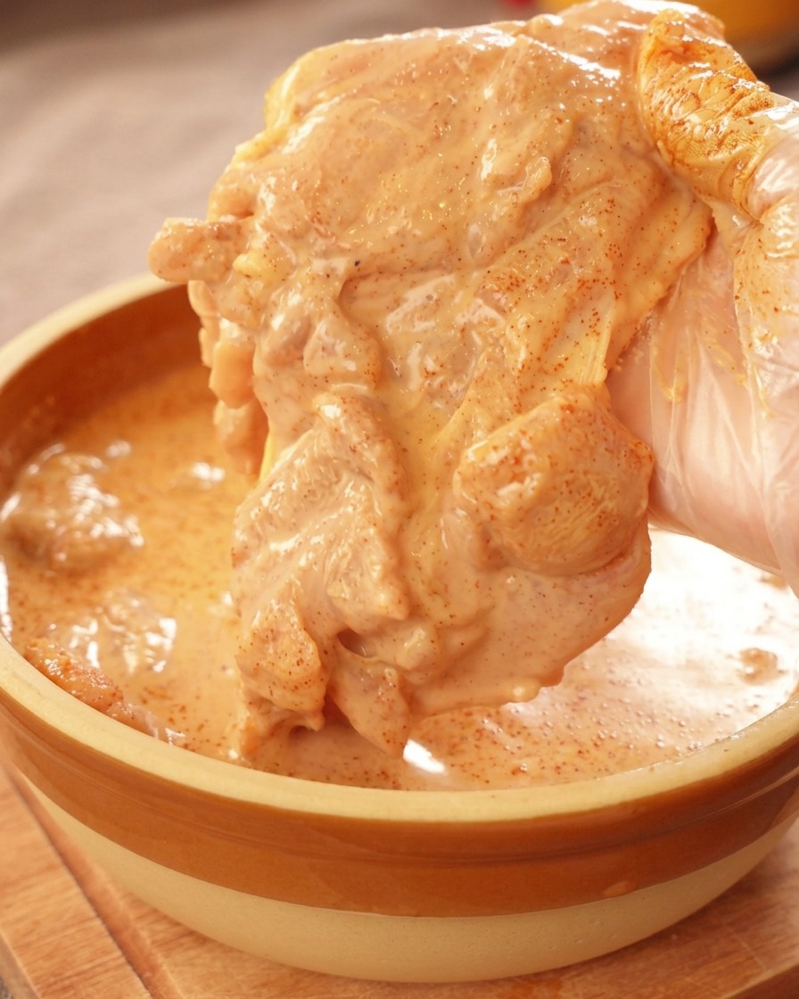 オレンジ色のマリネ液がしっかり絡んだ鶏もも肉を持ち上げている様子