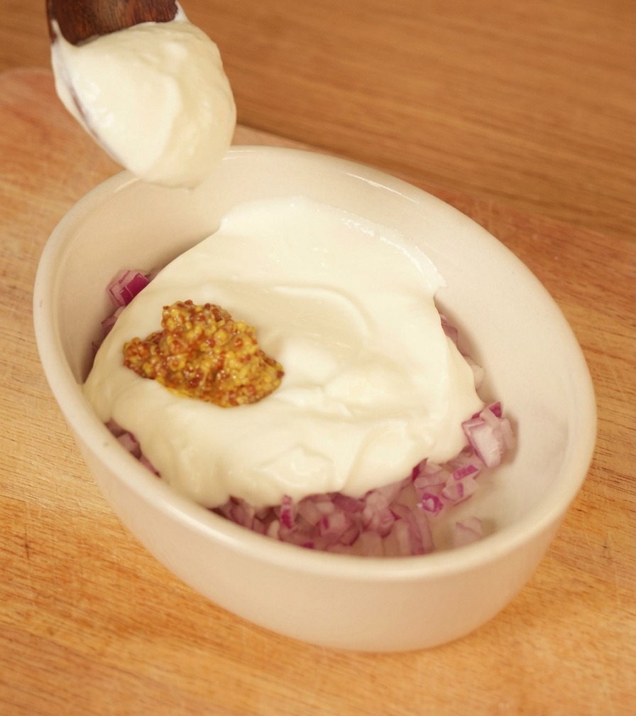 刻んだ赤玉ねぎと粒マスタードが入ったボウルにヨーグルトを加えている様子