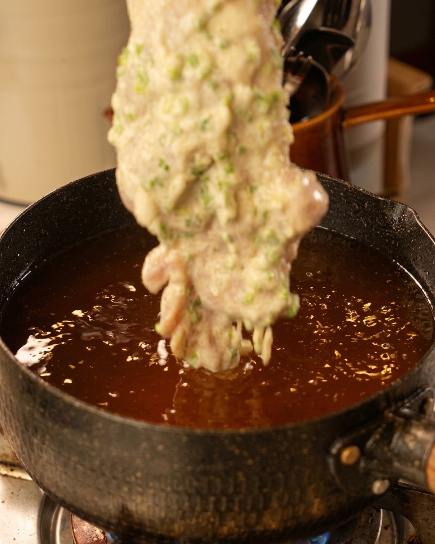 熱い油の中に衣をつけた鶏肉をそっと入れている様子