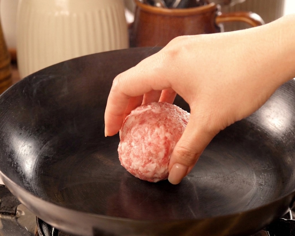 煙が立つほど熱くなった鉄製のフライパンに、丸めた肉をそっと置いている様子。