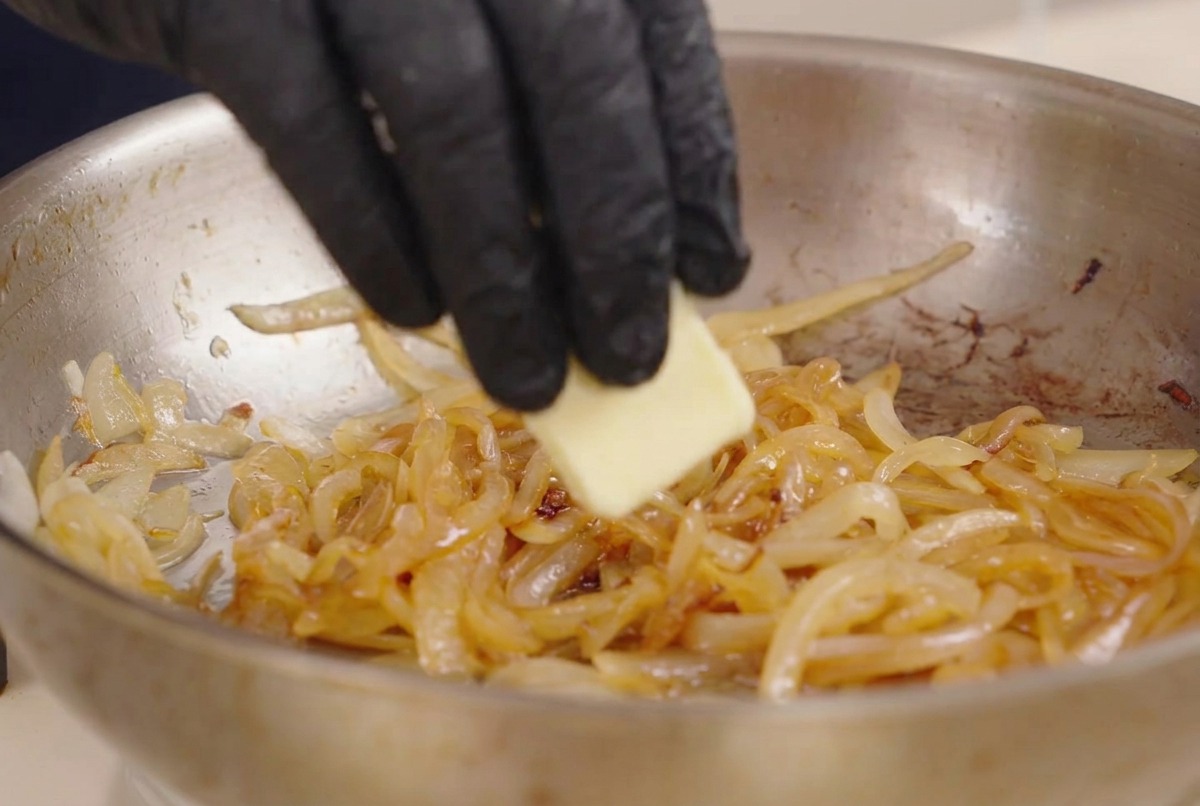 炒めたたまねぎと調味料が入ったフライパンに、バターを一片加えている様子。