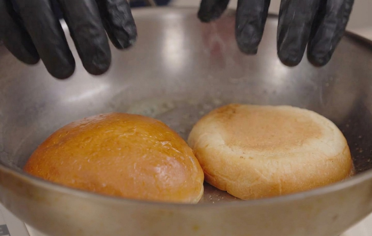 熱したフライパンで、バターを塗ったバンズの断面を押し当てて焼いている様子。