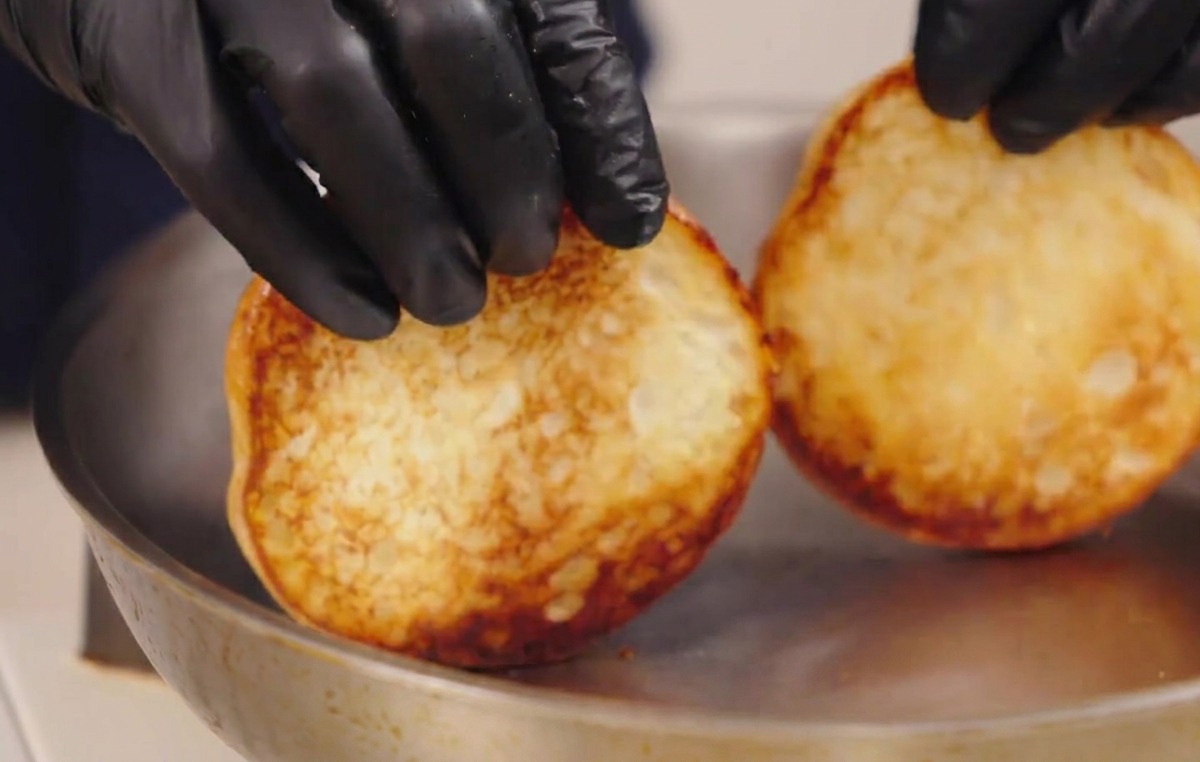 こんがりと黄金色に焼き上がったバンズをフライパンから持ち上げている様子。