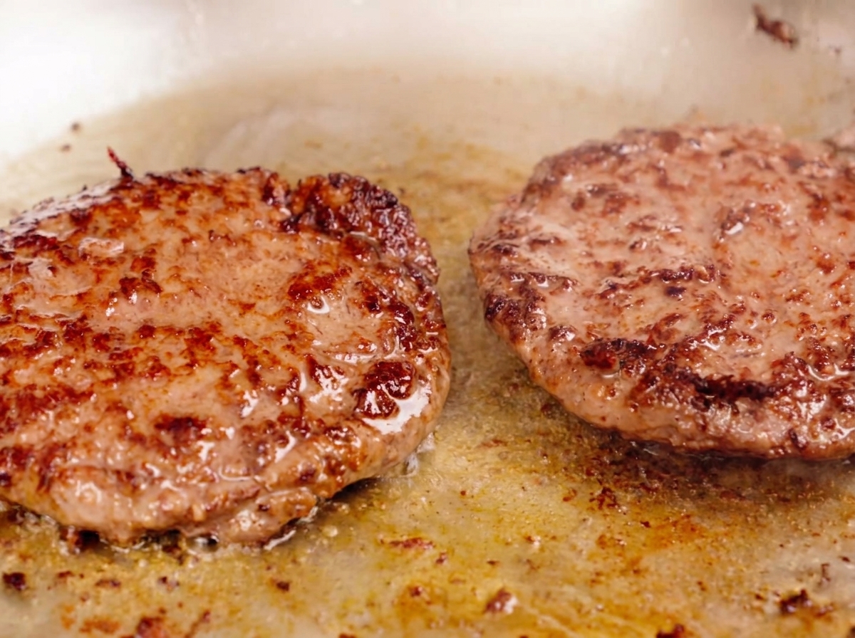 肉汁が溢れ出し、表面にしっかりとした焼き目がついた2枚の厚いパティを焼いている様子。