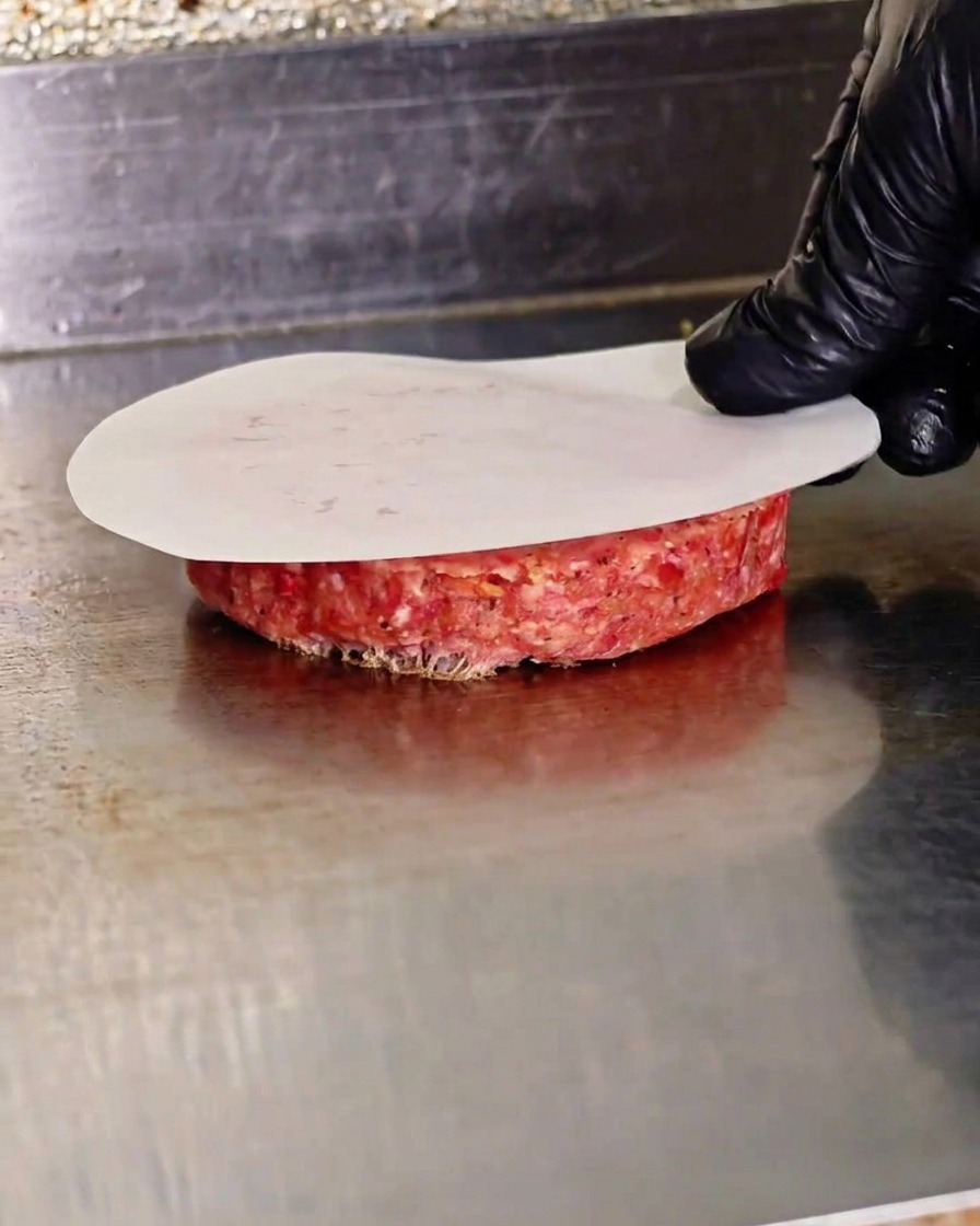 クッキングシート越しにプレス機でひき肉を平らに押し潰している様子。