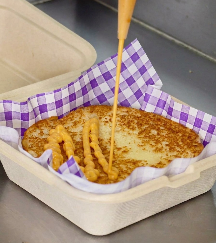 焼けたバンズにオレンジ色のソースを絞り出している様子。