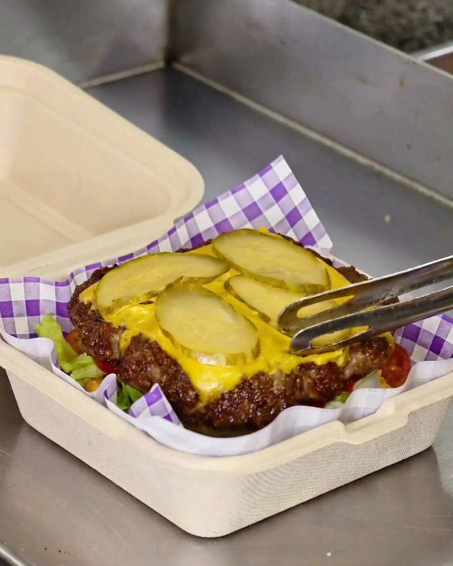 チーズとピクルスがのったパティを野菜の上に移動させている様子。