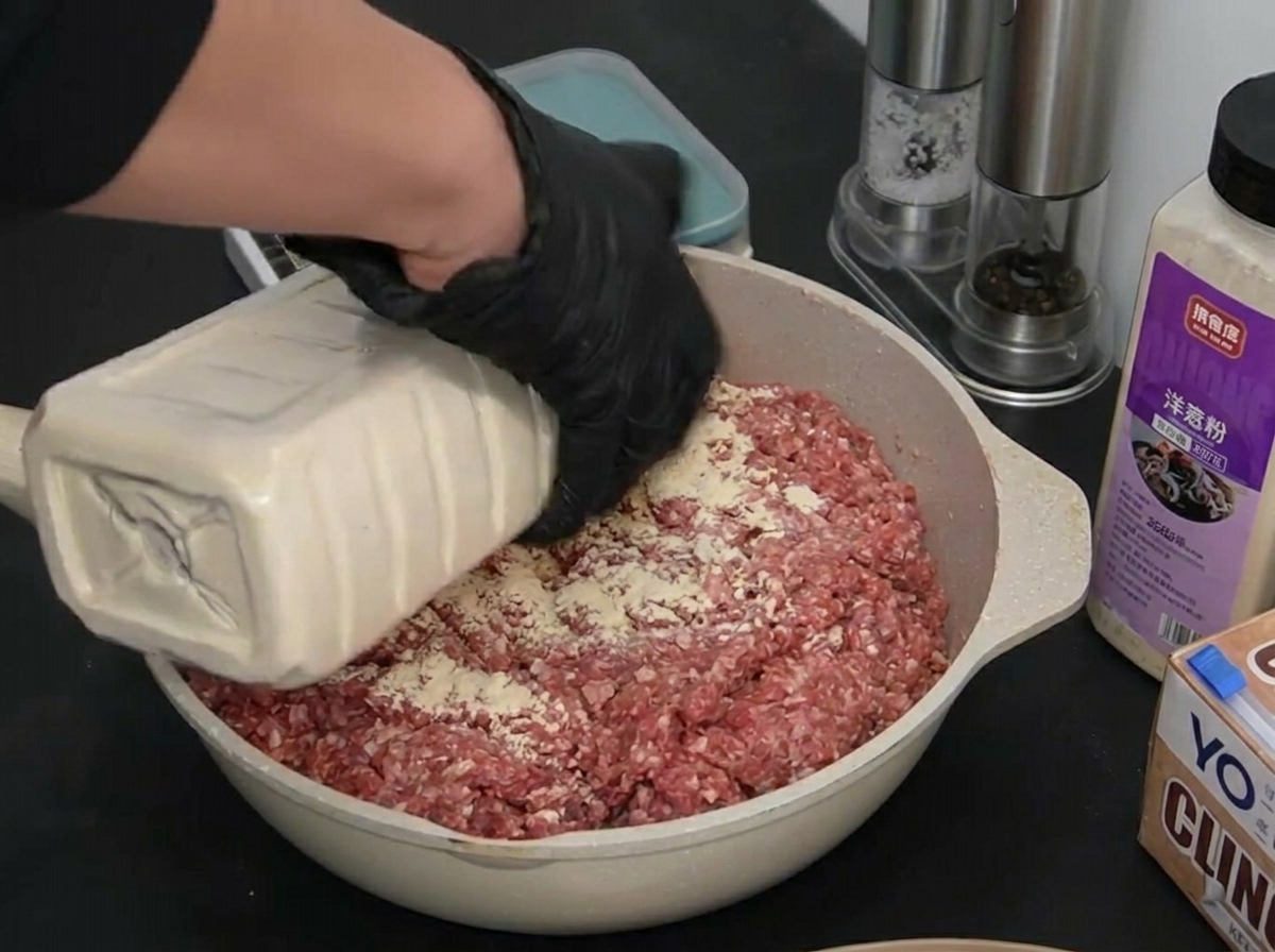 牛挽肉の上に白いガーリックパウダーを丁寧に振りかけている様子。