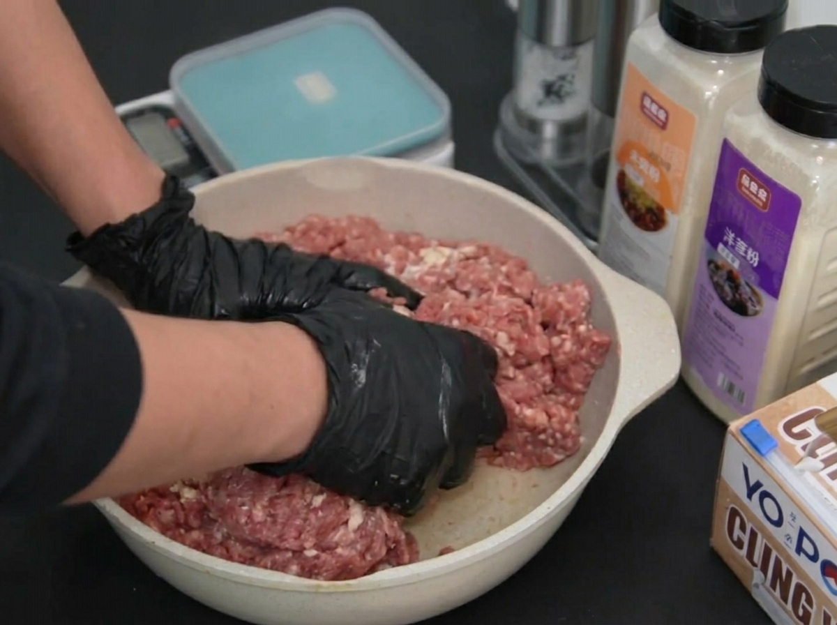 バットの中で両手を使って牛挽肉を力強くこね、混ぜ合わせている様子。