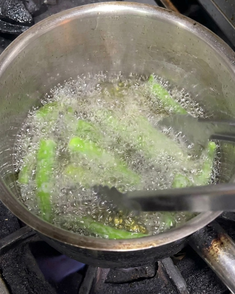 トングを使って、熱い油の中で泡を立てながら揚がっている丸ごとのグリーンチリ