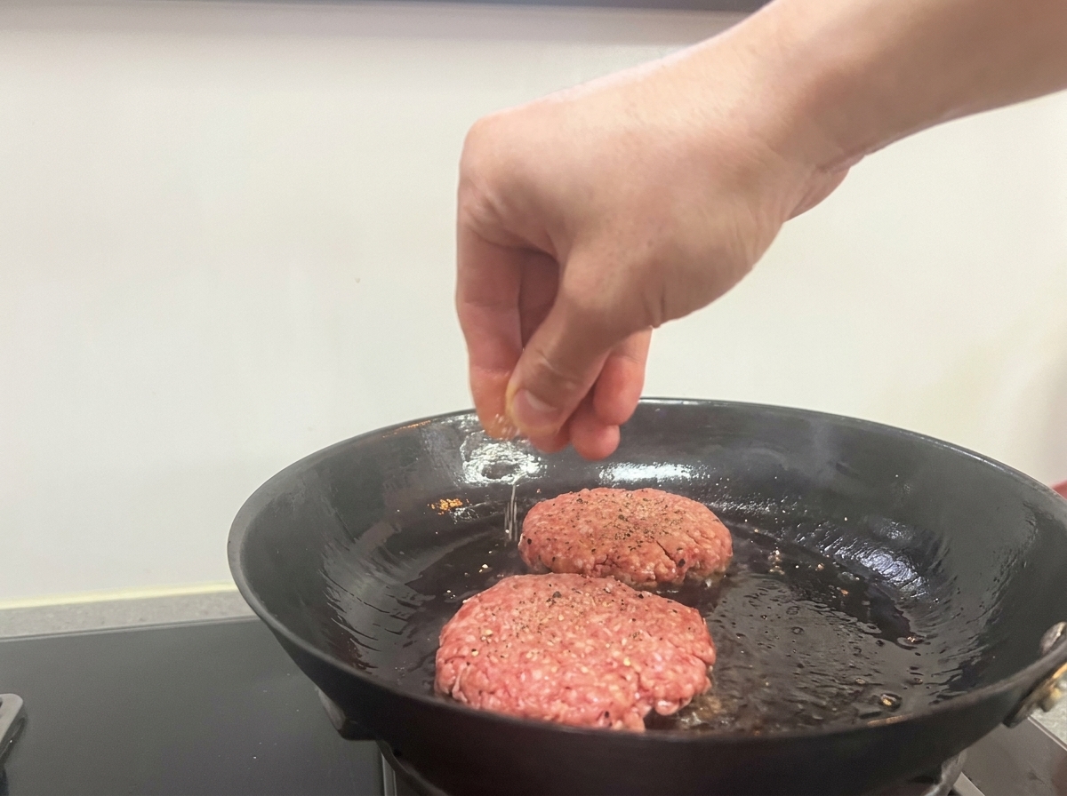 焼いているパティに塩こしょうを振る様子