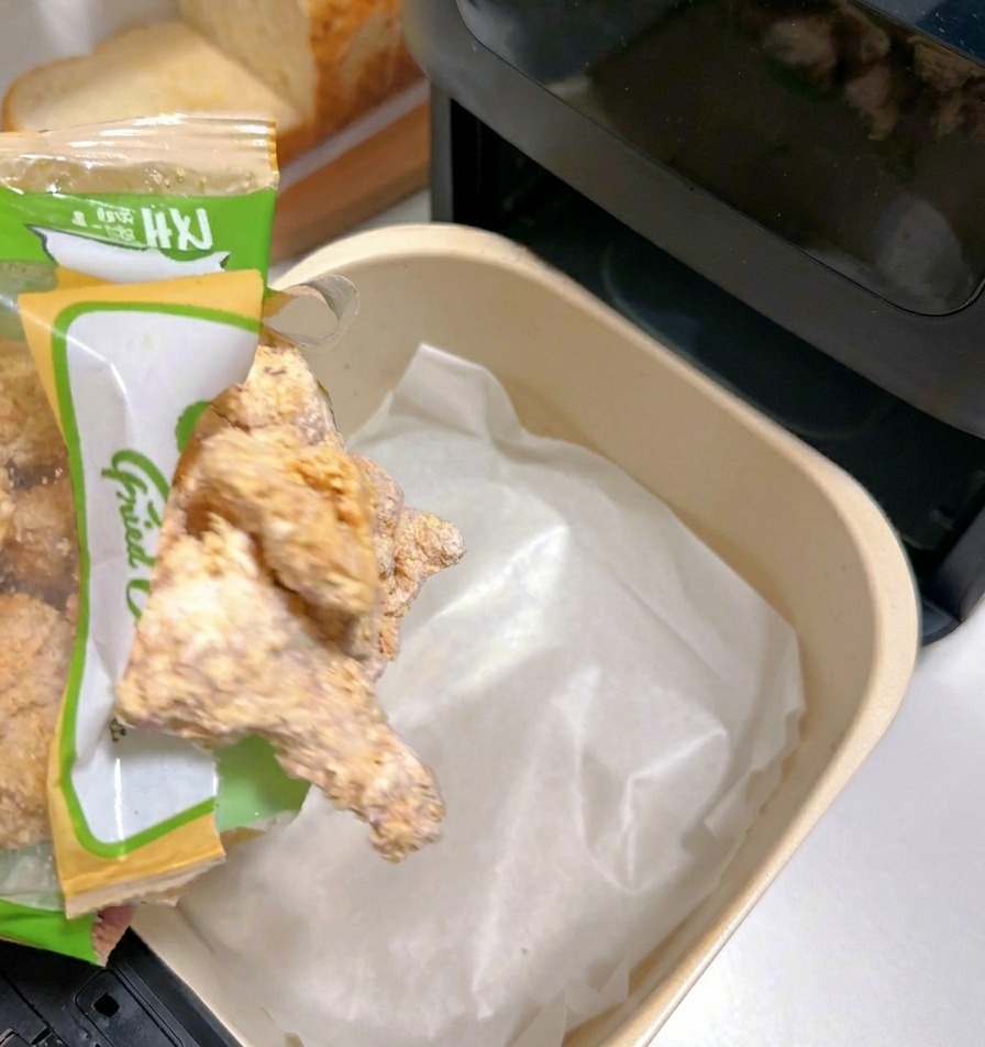 白いクッキングシートを敷いたエアフライヤーのバスケットに、冷凍の鶏唐揚げを並べている様子。