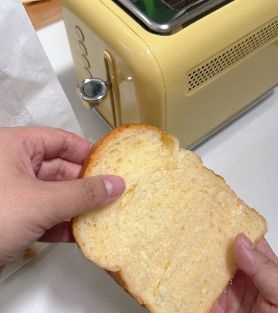 レトロな黄色いトースターに厚切りの食パンを差し込んでいる様子。