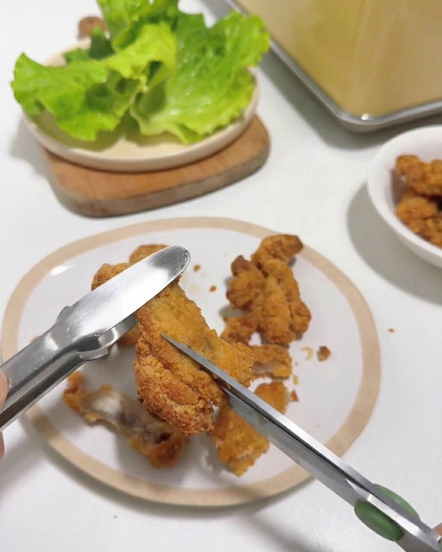 トングで押さえた熱々の唐揚げを、キッチンバサミで食べやすい大きさにカットしている様子。