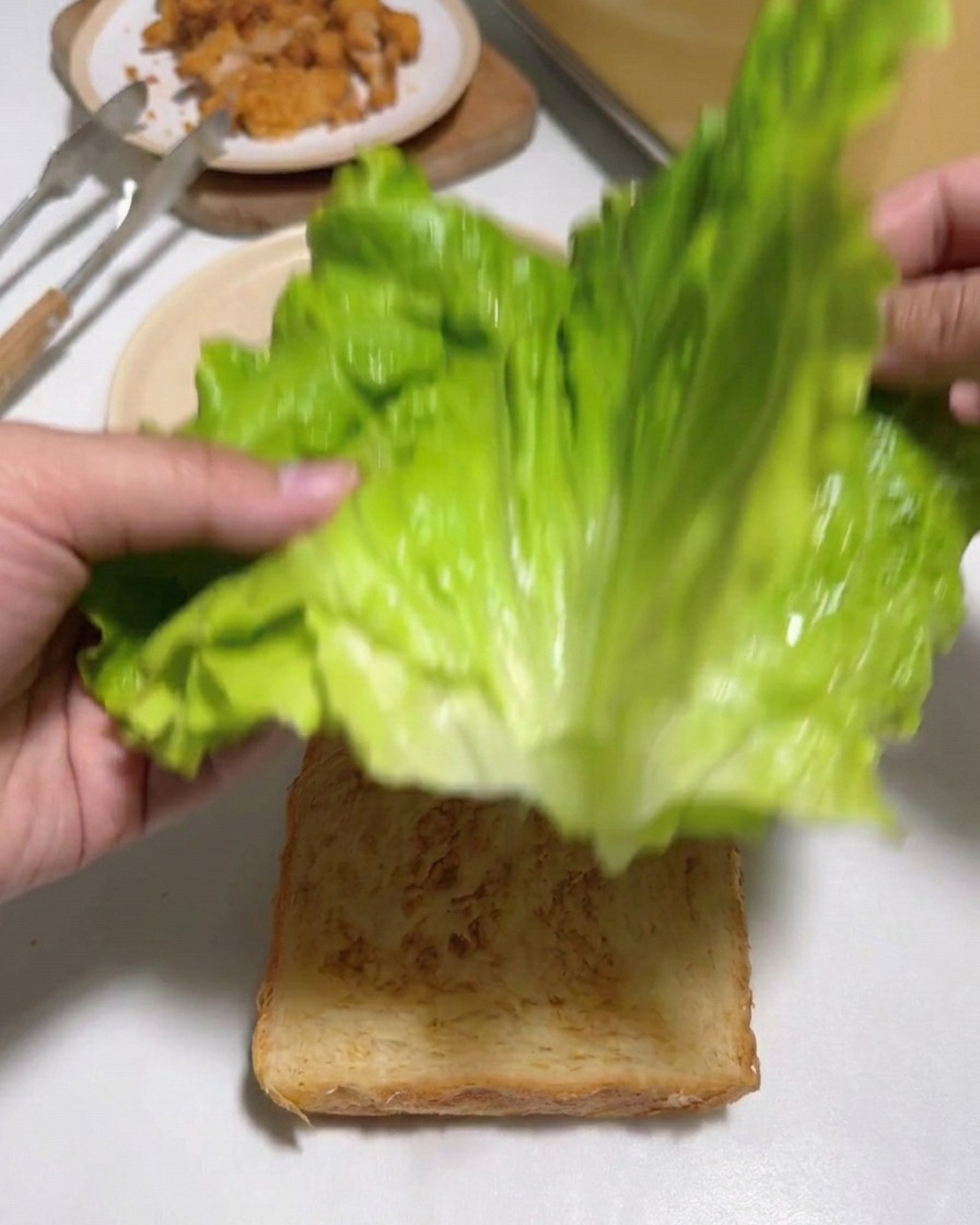 トーストした食パンの上に、新鮮な緑色のレタスを重ねて置いている様子。