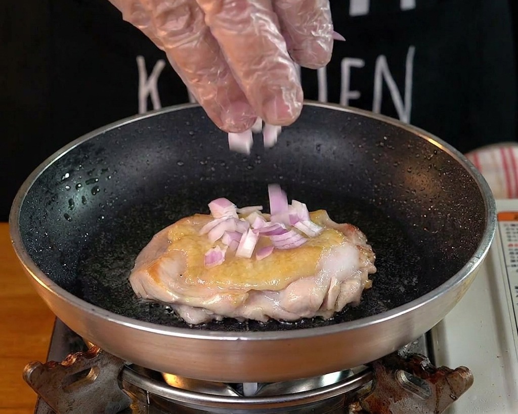 鶏肉を焼いているパンの隙間に赤玉ねぎのみじん切りを散らしている様子
